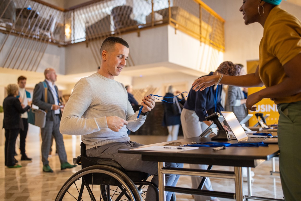 Man in a wheelchair collecting a lanyard at a conference