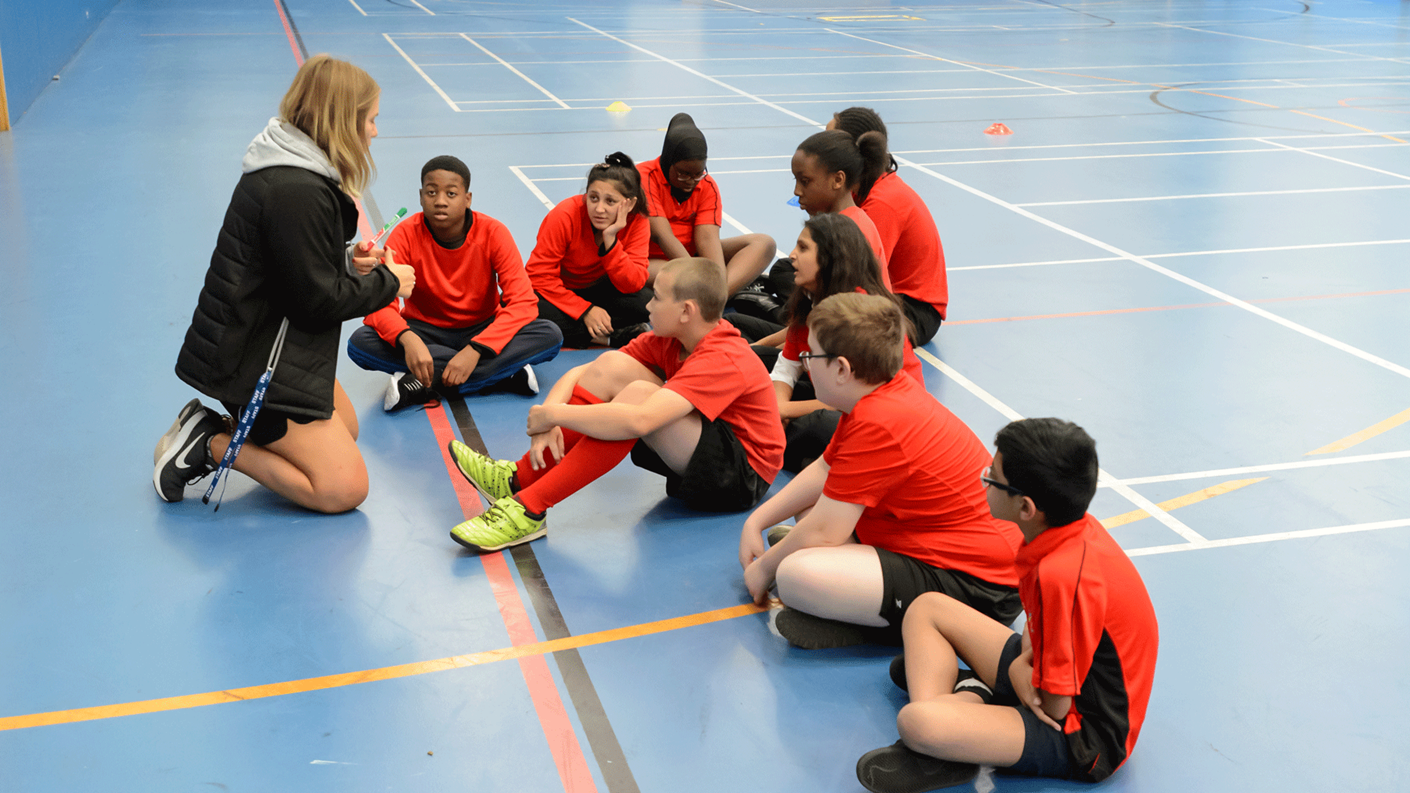 coach with teenagers seated in sports hall