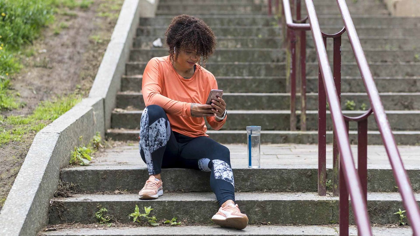 A woman in running gear sitting on some stairs looking at her phone