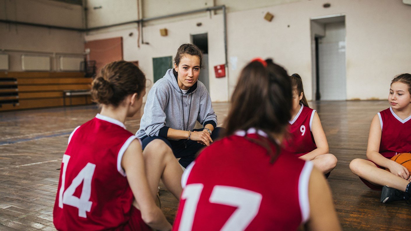 Coach in sports hall with teenagers sat on floor